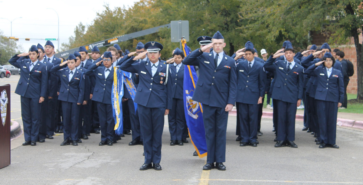 Uniformed cadets sauting in formation with flag