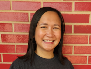 Image is of the SSA counselor. She is brunette and smiling, and is wearing a black shirt. She is standing in front of a red, brick wall. 