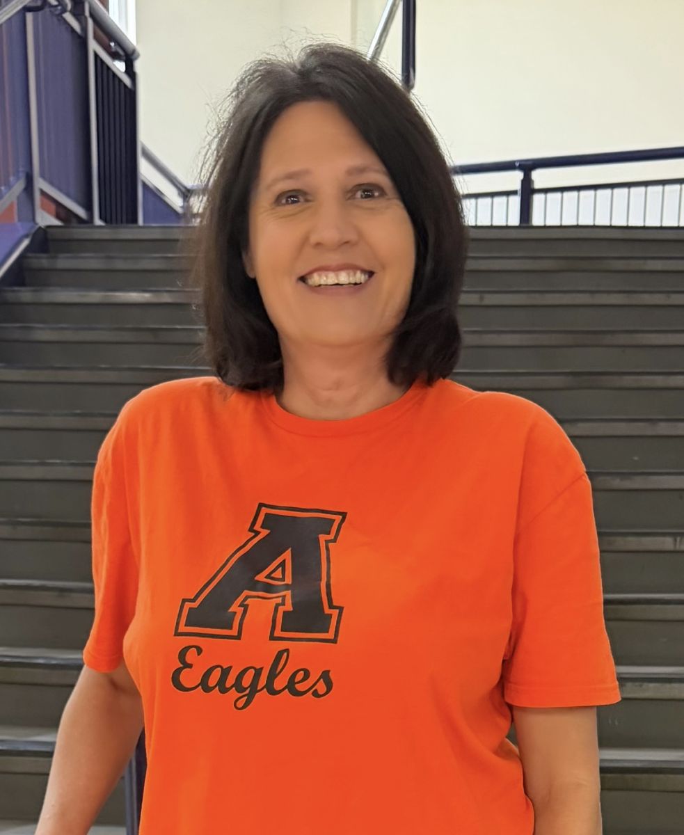Image is of the STEM counselor. She is brunette and smiling, and is wearing a bright orange shirt with a large A and eagles written below it.